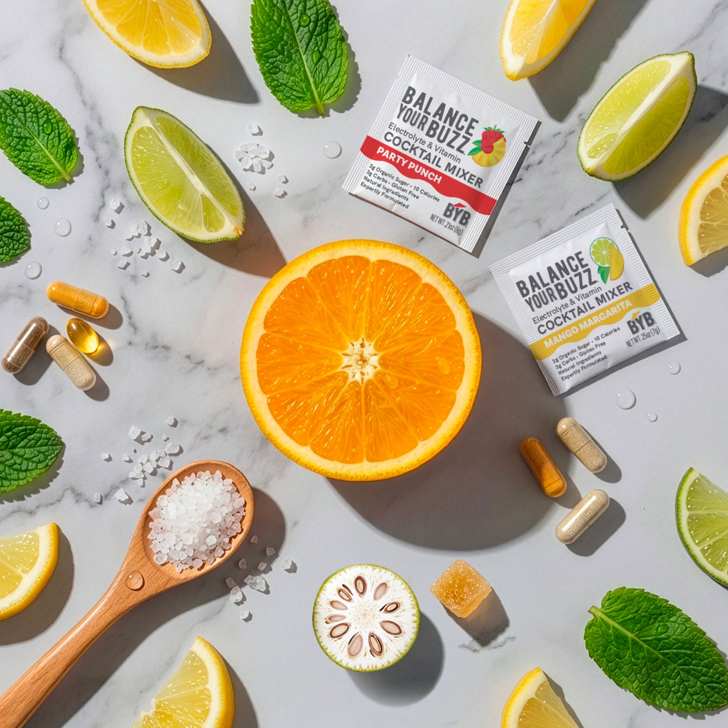 Cocktail mixer packets with citrus fruits, herbs, and candies on a marble surface